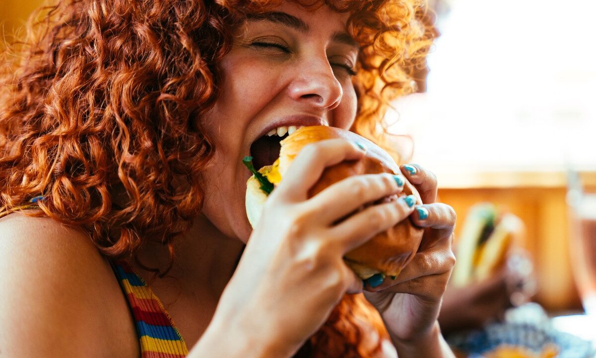 La ragazza addenta l'hamburger con un'espressione di puro piacere.