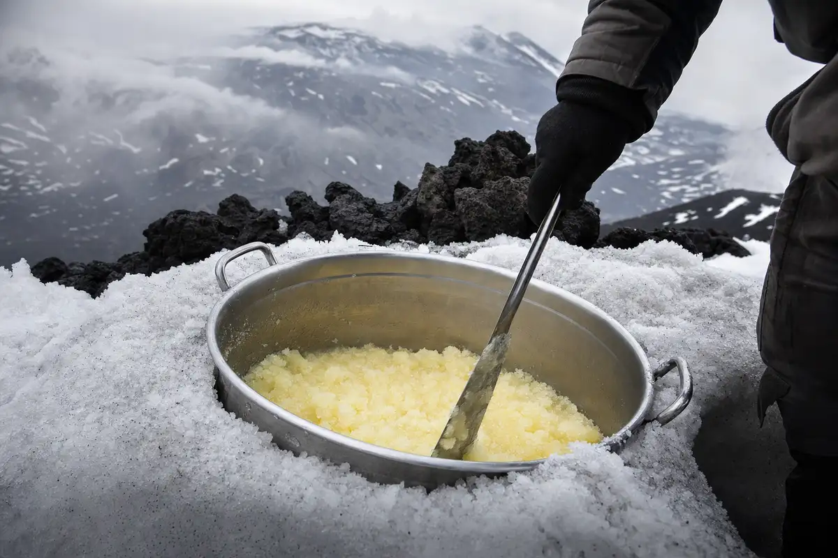 Carapina in metallo nella neve con granita al limone mescolata da una mano con guanto, tra rocce laviche e nebbia