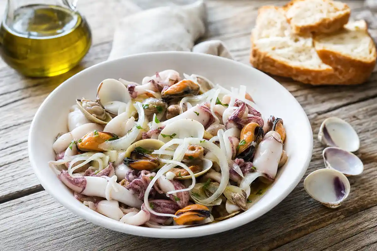 Insalata di mare cruda con calamaretti, cozze, vongole e cipolla in una ciotola bianca su tavolo rustico
