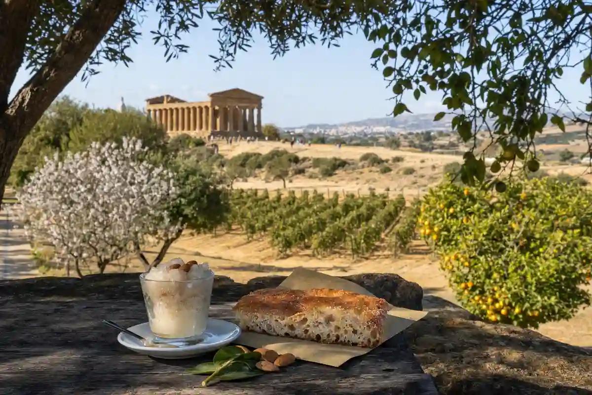 Granita di mandorla e focaccia su tavolo rustico con tempio greco sullo sfondo nella Valle dei Templi