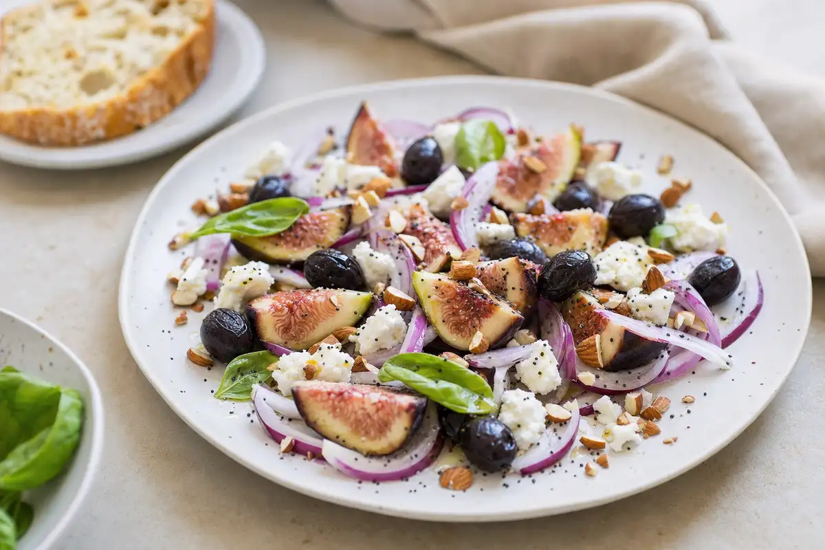 Insalata con fichi a spicchi, olive nere, cipolla rossa, caprino sbriciolato, mandorle e basilico su piatto