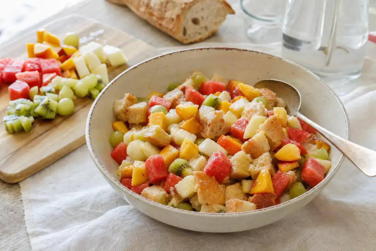 Ciotola di panzanella dolce con cubetti di pane e frutta estiva, con cucchiaio su tavolo chiaro