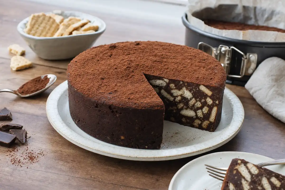 Torta fredda al cacao senza cottura con una fetta tagliata, su piatto chiaro, con pezzi di biscotti visibili