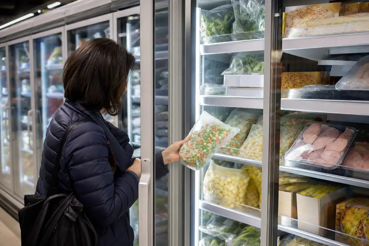 Cliente al banco surgelati di un supermercato mentre sceglie una busta di verdure miste dal freezer